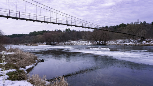 Winter landscape with river and suspended pedestrian bridge