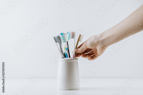 Hand takes eco friendly toothbrush from a white cup. White background with space for text. Dental care concept photo