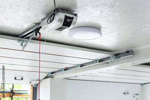Opening door and automatic garage door opener electric engine gear mounted on ceiling with emergency cord. Double place empty garage interior with rolling entrance gate