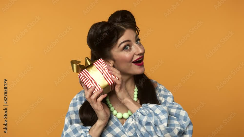 Shocked pin up woman holding gift box and smiling at camera Shocked pin up woman holding gift box and smiling at camera