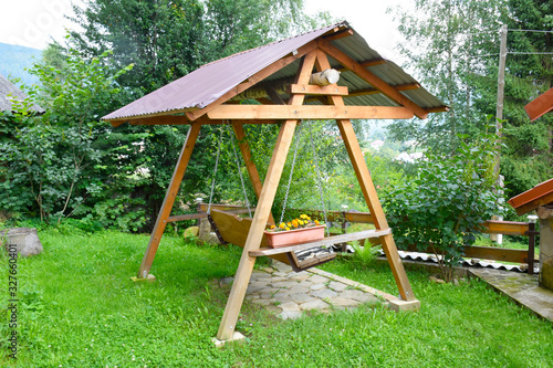 Massive old outdoor equipment swing chair with strong wooden frame, with cut grass and dense trees in suburban family house backyard.
