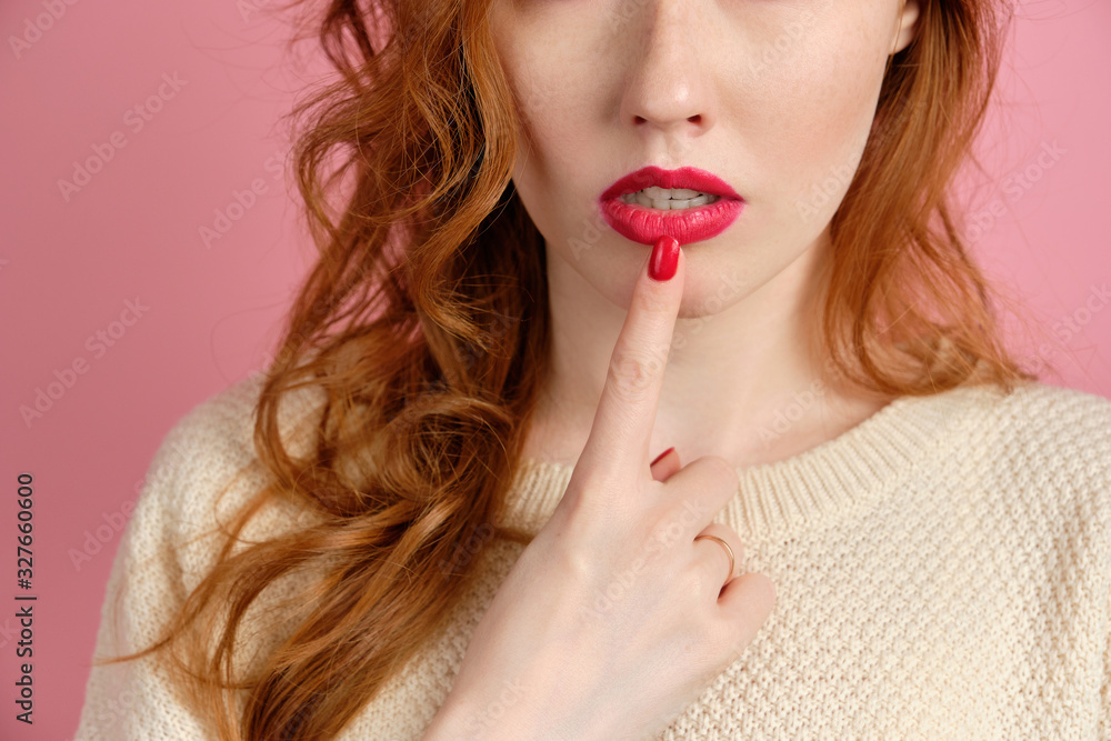 A close shot of the lips of a red-haired girl with red lipstick and a finger with red varnish at the mouth A close shot of the lips of a red-haired girl with red lipstick and a finger with red varnish at the mouth