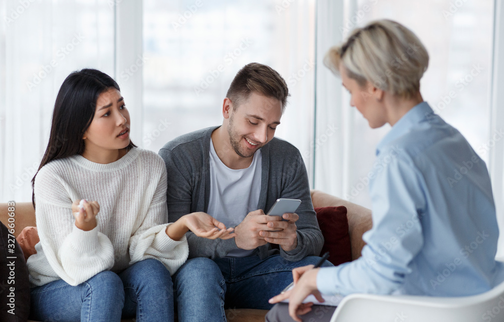 Wife Talking With Psychologist While Husband Using Smartphone In Office Wife Talking With Psychologist While Husband Using Smartphone In Office
