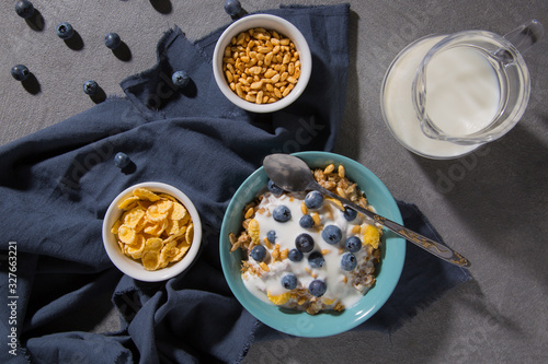 Bowl with granola and yogurt, cornflakes, blueberries and a glass of milk on a gray background
