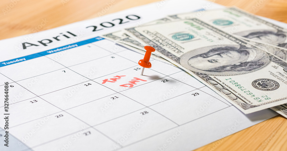 Red pin marked at April 15 for tax day with dollars falling on 2020 calendar. Red pin marked at April 15 for tax day with dollars falling on 2020 calendar.