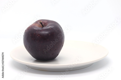 Dark red apple on a white plate isolated on a white background.