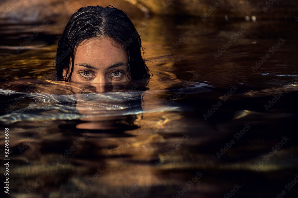 Joven mujer morena con la mitad de su rostro y su cuerpo sumergido en el agua mirando hacia adelante con sus hermosos ojos Joven mujer morena con la mitad de su rostro y su cuerpo sumergido en el agua mirando hacia adelante con sus hermosos ojos