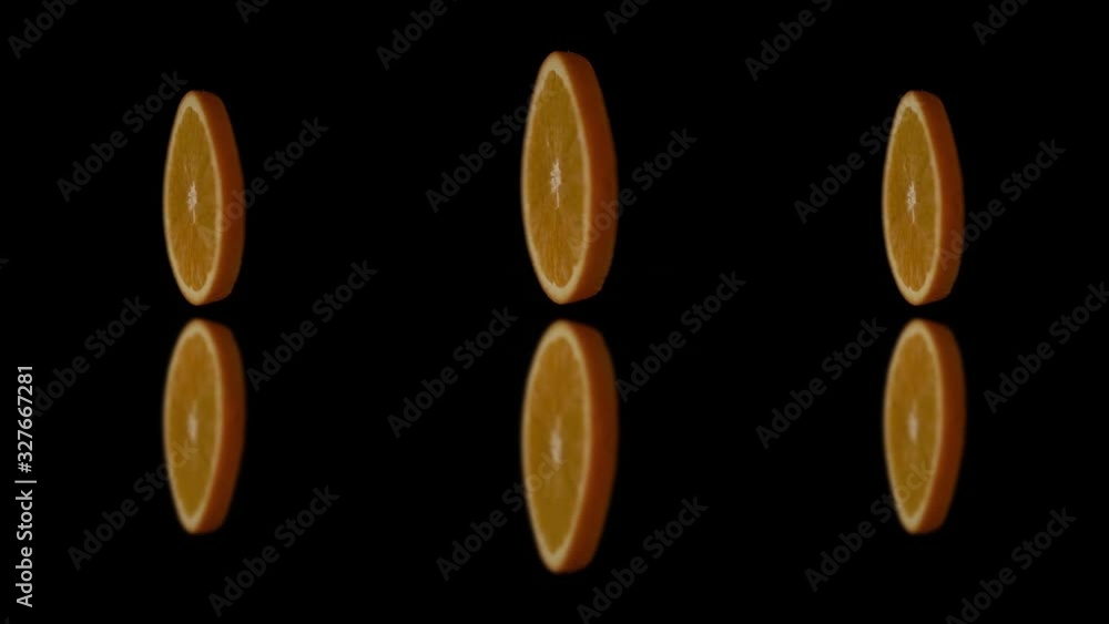 Round Three slices of ripe orange rotate on a black background. Orange segments are turned on the mirror surface. Slices of oranges hung in the air and quickly spinning. Round Three slices of ripe orange rotate on a black background. Orange segments are turned on the mirror surface. Slices of oranges hung in the air and quickly spinning.