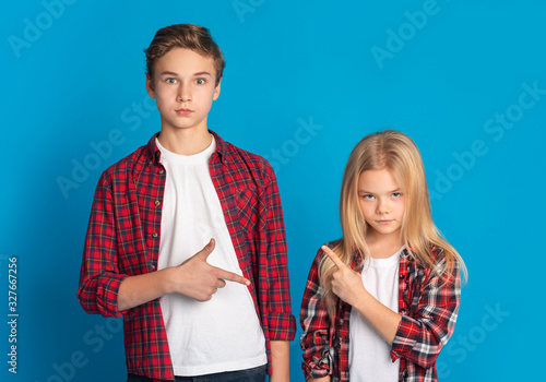 Siblings pointing at each other, accusing and blaming on blue background photo