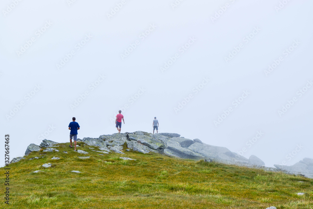 Guys stand on top surrounded by fog and low clouds near Transalpina road in Romania.
