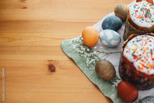 Stylish easter eggs natural dyed and homemade easter cake on rustic cloth with flowers and green brunches on wooden table. Happy Easter. Traditional Easter food. Copy space