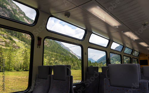 Swiss train interior with comfortable chairs, on two rows, a table and mountain, foresrs view on window. Public transport. Passenger train interior © bbgreg