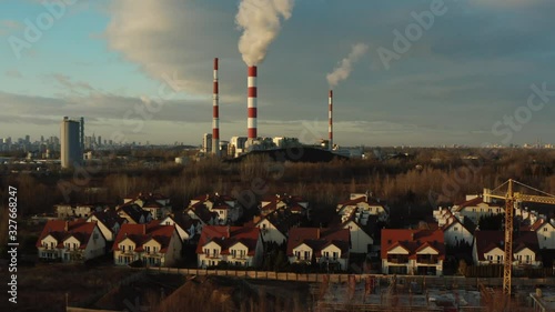 Aerial view of a heat power plant with pipes at sunset. Steam, smoke from pipes at a thermal power station.  European village on the background of chimneys.