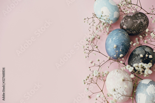 Happy Easter composition. Stylish easter eggs and spring flowers border on pink paper flat lay, space for text. Modern natural dyed blue and marble easter eggs. Card template