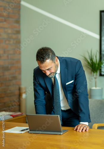 The boss, who checks and takes notes at the computer in his own workroom in the office, the handsome hardworking boss with the beard in the suit, the bank manager, the team leader