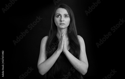 Black and white portrait of a young woman who prays. Folded hands in prayer.