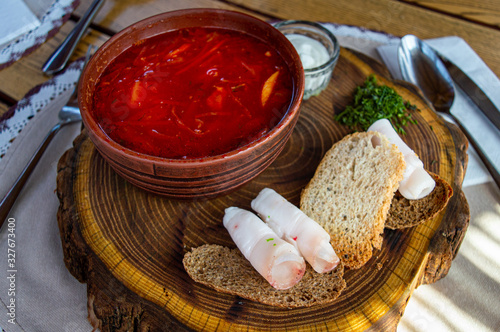 Beet soup in ceramic plate with becon, bread and sour cream on wooden board. Borch, traditional Ukrainian food photo