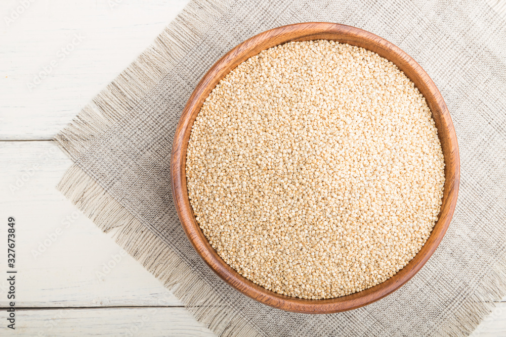 Wooden bowl with raw white quinoa seeds on a white wooden background. Top view, close up.