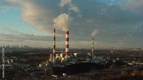 Aerial view of a heat power plant with pipes at sunset. Steam, smoke from pipes at a thermal power station.  European village on the background of chimneys.