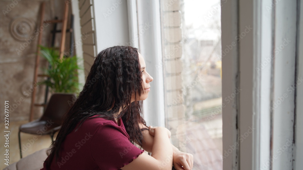 A beautiful woman looks out the window and about something thinks or dreams. Woman in casual wear