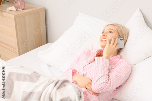 Young woman talking by mobile phone in bedroom