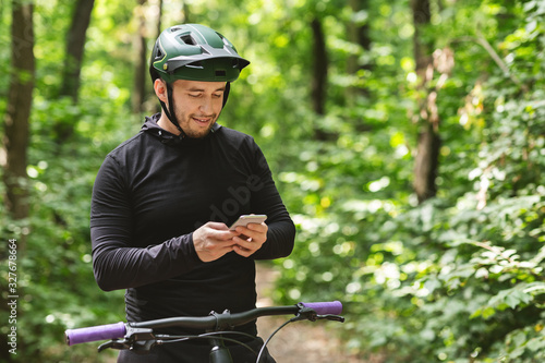 Fototapeta Naklejka Na Ścianę i Meble -  Happy cyclist holding smartphone, checking on messages