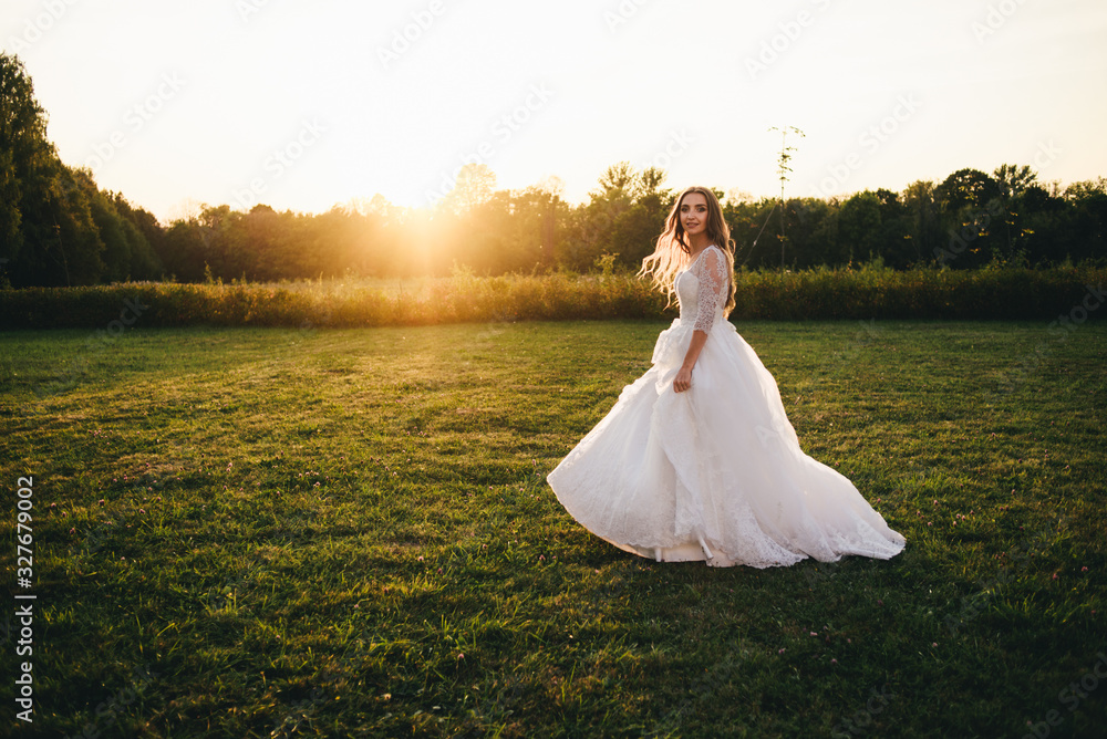 Beautiful young woman in a white wedding dress and black boots at sunset is photographed.