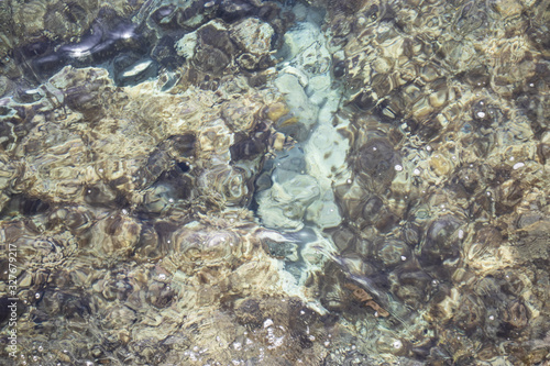 Turquoise Water near to the Sand underneath forming many little waves reflecting the Sun