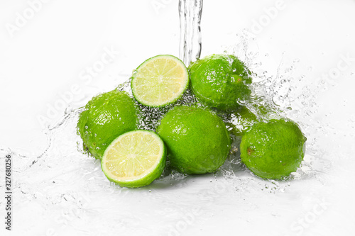 Water pouring on fresh limes against white background