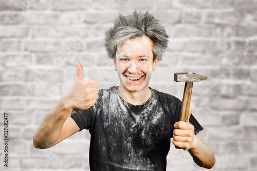 Dirty young builder guy in plaster is hold a hammer on brick wall background at home during repairs