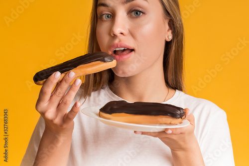 Young Woman Eating Eclairs With Chocolate Cream And Looking At Camera