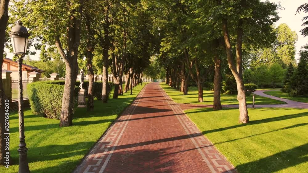 Moving over red cobblestone alley in the park. Trees and pole lamps. Daylight shadows. Moving over red cobblestone alley in the park. Trees and pole lamps. Daylight shadows.