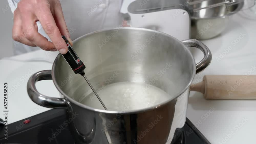 A girl baker, in uniform, measures the temperature with a thermometer in syrup for baking cakes and desserts for the holidays. A girl baker, in uniform, measures the temperature with a thermometer in syrup for baking cakes and desserts for the holidays.