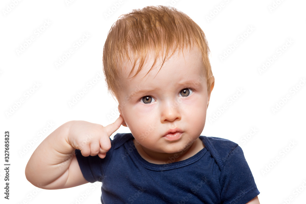 toddler with red hair in dark blue clothes looks into the frame with his eyes and holds his finger to his ear indicating a conditional sign to hear or not to listen isolated on a white background. toddler with red hair in dark blue clothes looks into the frame with his eyes and holds his finger to his ear indicating a conditional sign to hear or not to listen isolated on a white background.