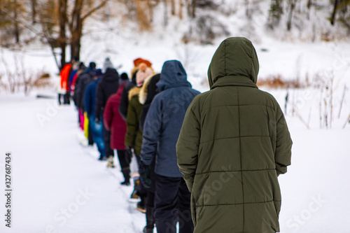 The lined up in one chain folk which is going to the winter camping in the forest. A large line of walking people in the forest