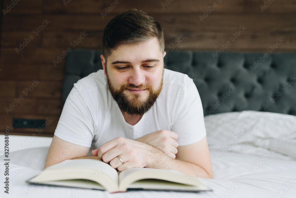 Close up young handsome caucasian man reading a book lying in bed Close up young handsome caucasian man reading a book lying in bed