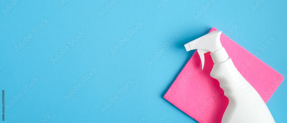 Cleaner spray bottle and pink rag on blue background. Cleaning service banner mockup. Housecleaning and housekeeping concept. Flat lay, top view - obrazy, fototapety, plakaty 