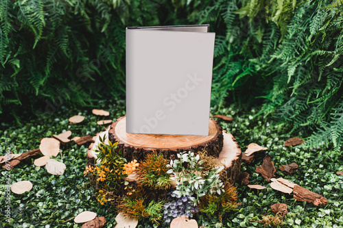 Book cover mockup on green background with tree logs, dry leaves and flowers. Book mockup on garden concept. Blank book. Book set on tree logs. Front view.