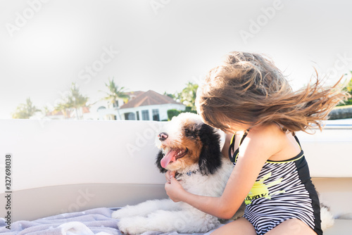 Young girl holding her puppy on a boat on a windy summer day photo