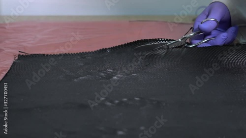 Specialist worker in coamposite with white coat and gloves, cutting carbon fiber with special scissors, in the workshop.