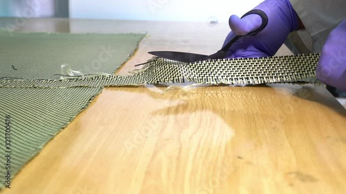 Worker Specialist in composite with white coat and gloves, cuts carbon / kevlar fiber using special scissors, in the workshop..