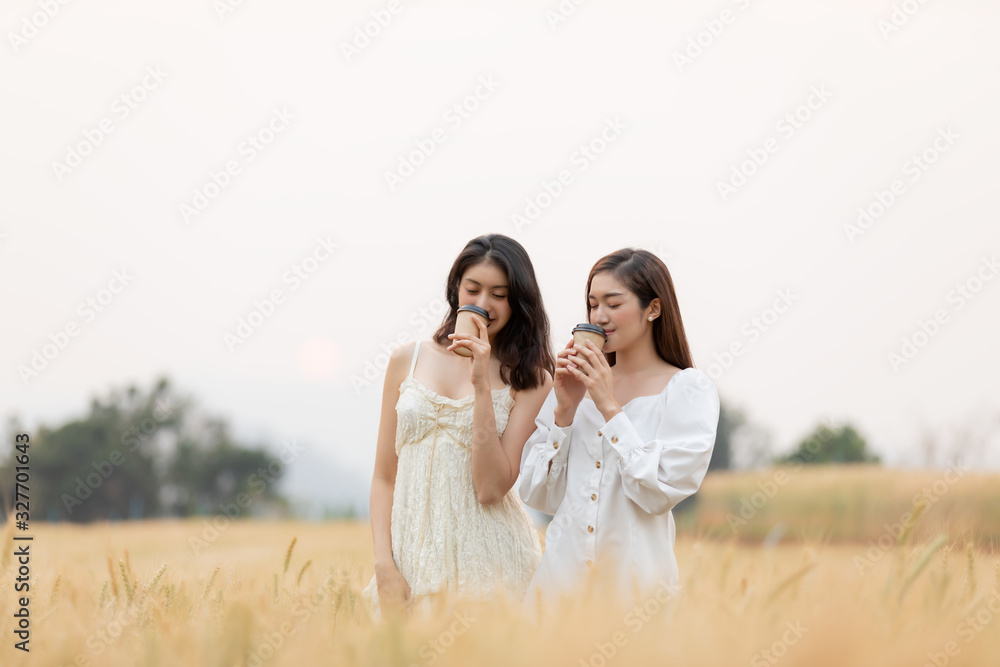 Two female friends holding takeaway coffee cup and having fun at barley field land in the morning.Happy time. Two female friends holding takeaway coffee cup and having fun at barley field land in the morning.Happy time.