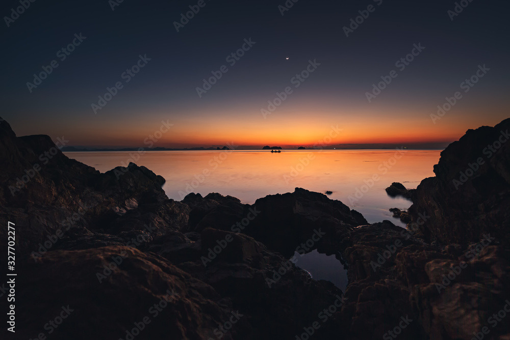Spectacular sunset and half moon over sea and boat on the rocky tropical beach Spectacular sunset and half moon over sea and boat on the rocky tropical beach
