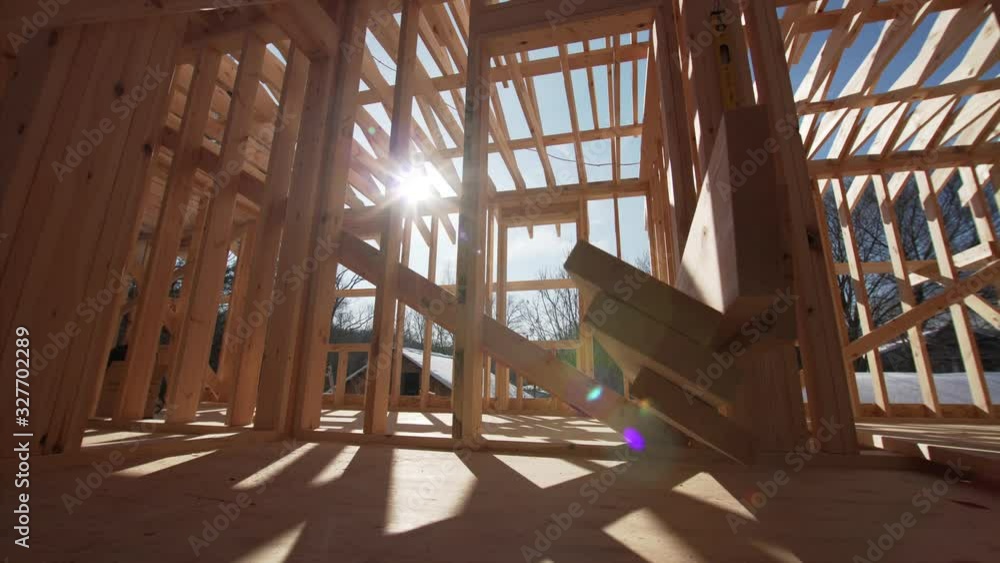 Sliding view of interior of empty room of the house under construction. Wooden planks on the floor. Bright sun is shining through the walls beams Sliding view of interior of empty room of the house under construction. Wooden planks on the floor. Bright sun is shining through the walls beams