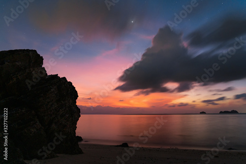 Dramatic sunset sky with stars and moon over rock by the sea at sunset