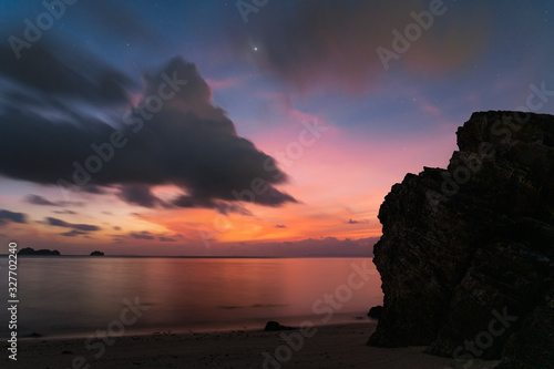 Dramatic sunset sky with stars and moon over rock by the sea at sunset
