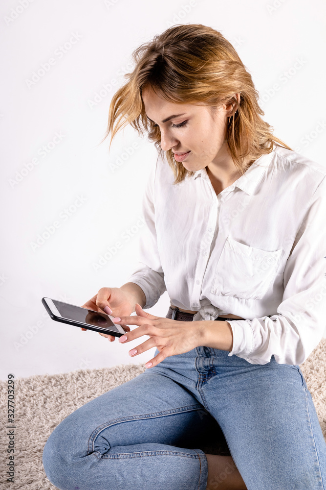 cute young girl in a white shirt looks at the smartphone with a slight smile