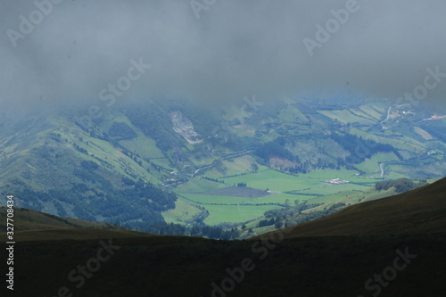 A valley seen from the mountain top that is covered in dark grey thunder clouds