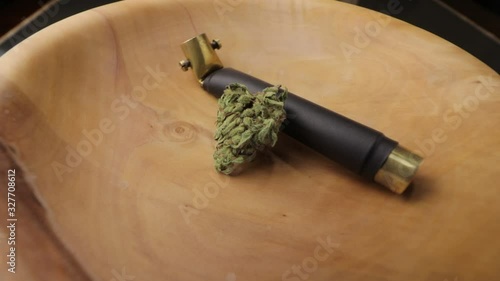 Brass smoking pipe with sativa and indica weed bud in wooden plate on the turning subject table. Low angle, closeup