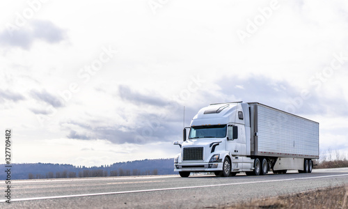 Industrial transportation big rig white semi truck transporting frozen cargo in reefer semi trailer running on the road with cloudy sky